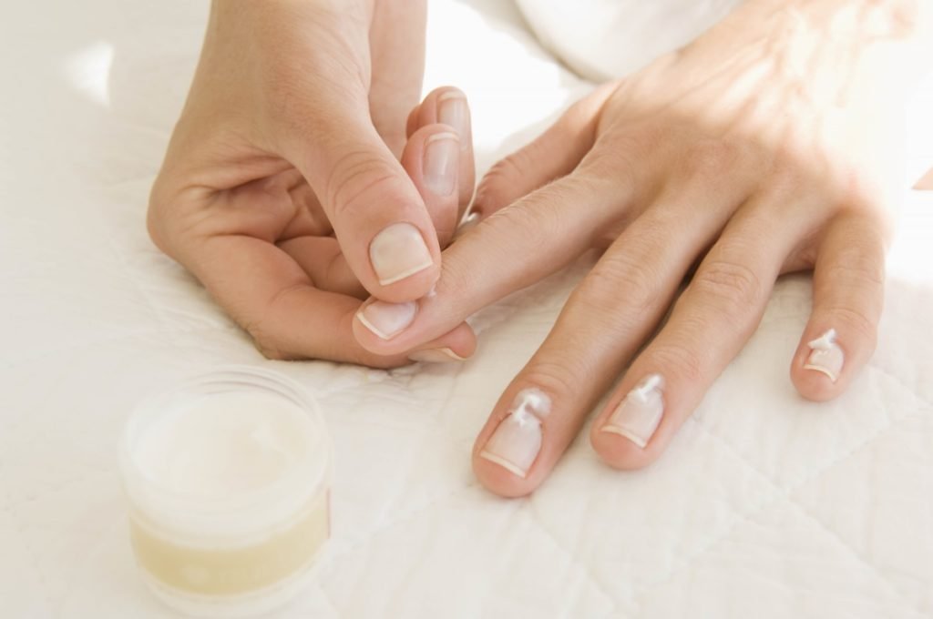 Mãos de uma mulher branca e jovem passando hidratante nas unhas. - Metrópoles
