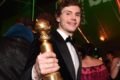 Evan Peters exibe o troféu do Globo de Ouro. Ele tem cabelo grande e loiro, veste um terno com gravada borboleta e sorri - Metrópoles