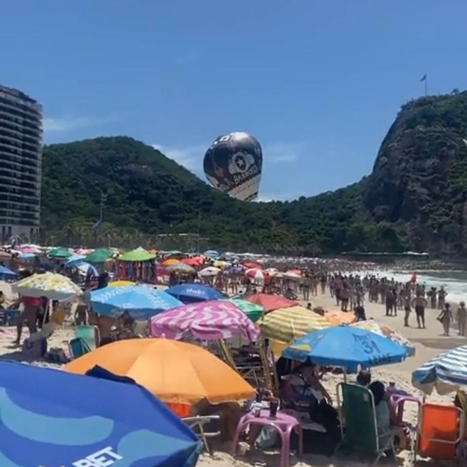 guardas-dois e pessoas em praia com morro e balão ao fundo - metrópoles