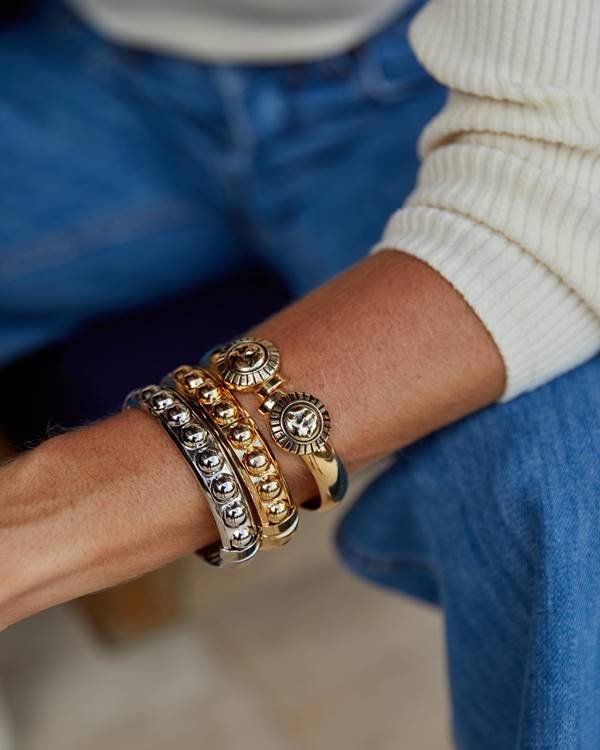 Foto de modelo branca com foco no braço com pulseiras douradas de prateadas - Metrópoles 