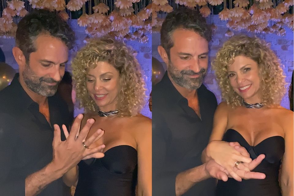 A foto colorida mostra Bárbara Borges e Iran Malfitano sorrindo de mãos dadas. Os dois olham para as mãos entrelaçadas com os aneis de compromisso
