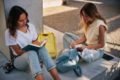 Duas adolescentes brancas, com cabelo liso, sentadas no chão estudando. Elas usam calças jeans e blusas beges e escrevem em cadernos. - Metrópoles