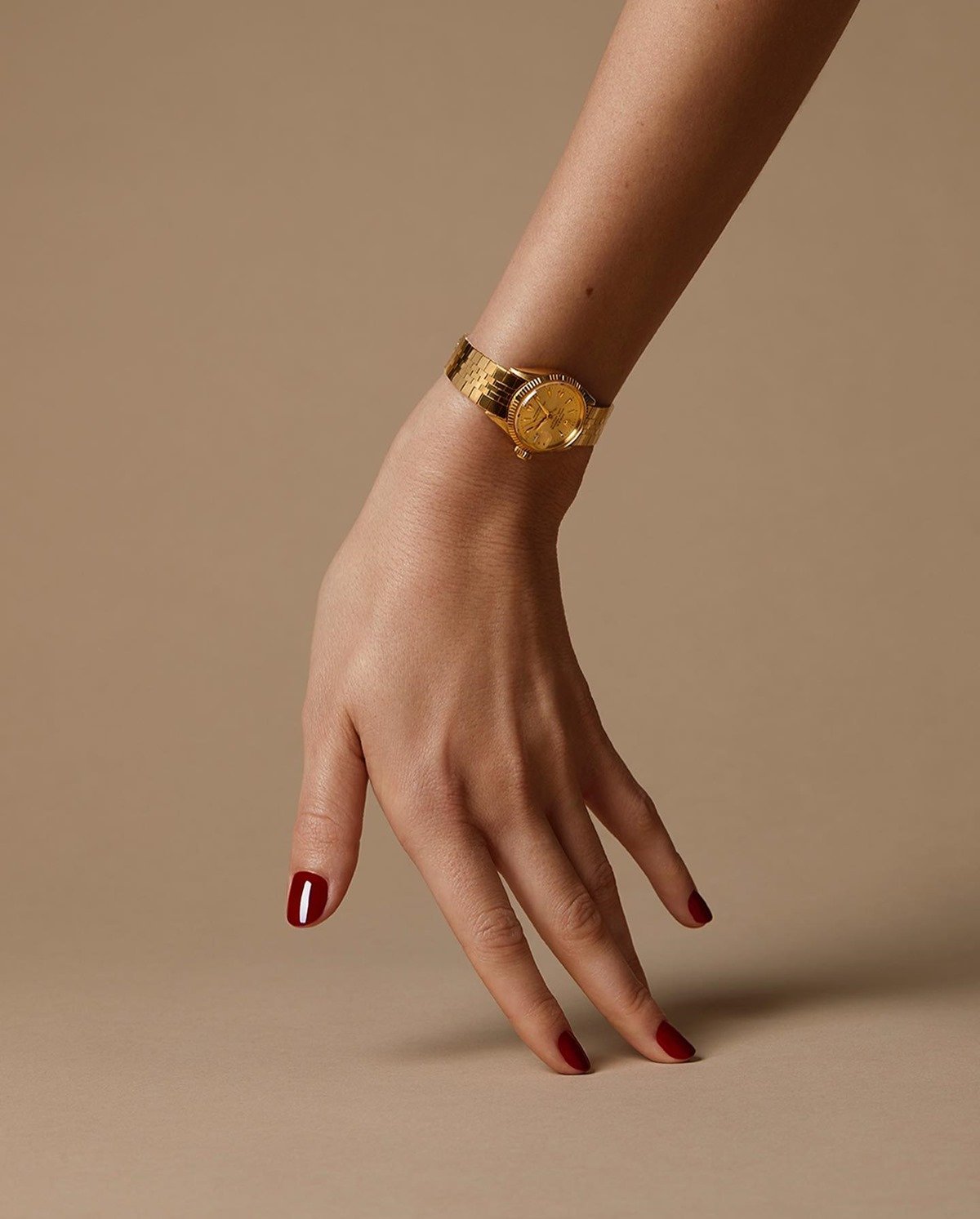 Mão de uma mulher branca e jovem, com unhas curtas e vermelhas, posa para foto usando um relógio da marca Rolex. A pela é dourada e bem delicada. - Metrópoles