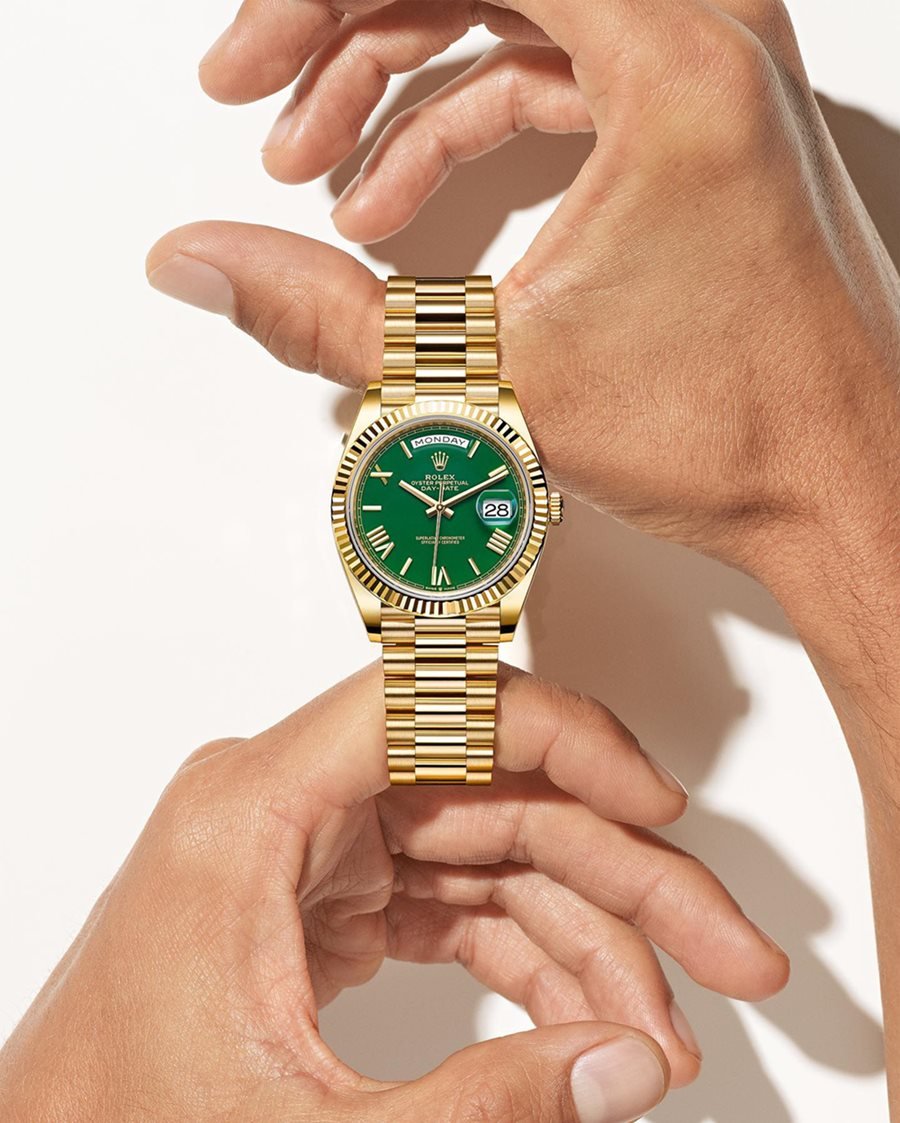 Mão de uma mulher branca e jovem, com unhas curtas, posa para foto usando um relógio da marca Rolex. O relógio é dourado com a caixa verde. - Metrópoles