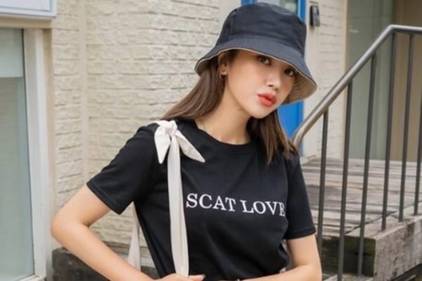 Na imagem, modelo asiática usa chapéu e camiseta preta com a escrita 