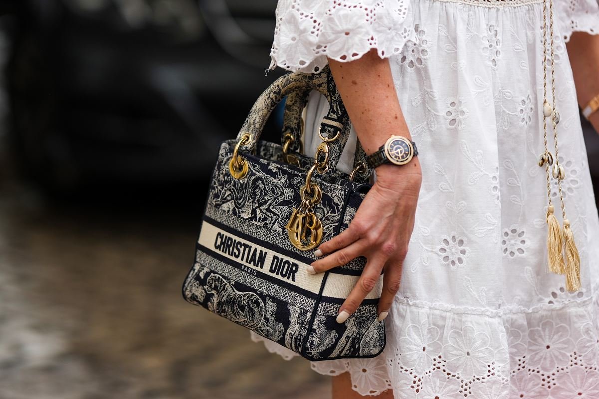 Bolsa Lady Dior, da marca Dior. A peça é feita em um tecido, com estampa preta e branca, e um pingente dourado com as letras C e D. - Metrópoles