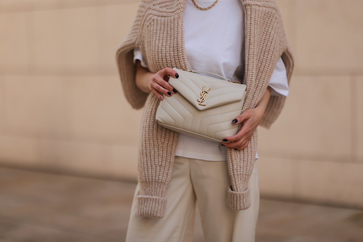 Mulher branca segura a bolsa Loulou, bege e de couro, da marca Saint Laurent. - Metrópoles