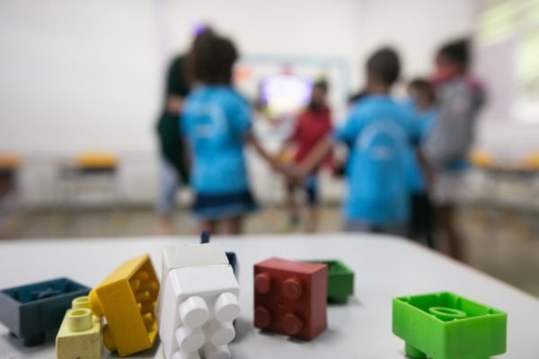 Foto colorida de blocos de montar em sala de aula com crianças ao fundo - Metrópoles