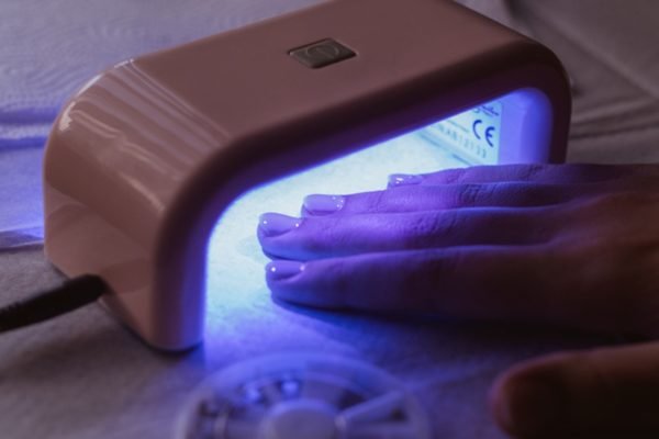 Imagem colorida: mão de mulher dentro de máquina de secar esmalte - Metrópoles