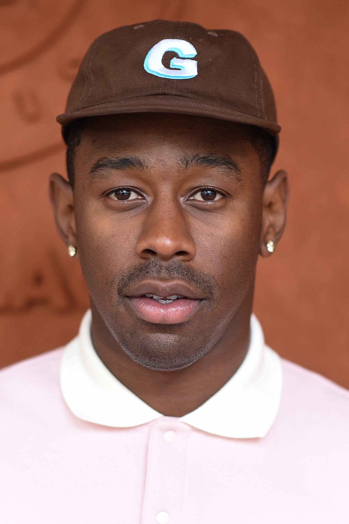 O rapper Tyler, The Creator, um homem negro e jovem, de cabelos raspados. Na imagem, ele usa uma camisa branca de botão e um boné marrom. - Metrópoles