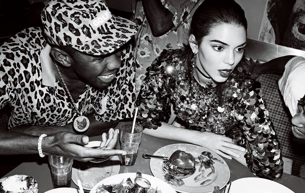 O rapper Tyler, The Creator, um homem negro e jovem, de cabelos raspados, posa para foto do lado da Kendall Jenner. A modelo é uma mulher jovem e branca, de cabelos pretos lisos. Eles estão conversando sentados em uma mesa de um restaurante. - Metrópoles