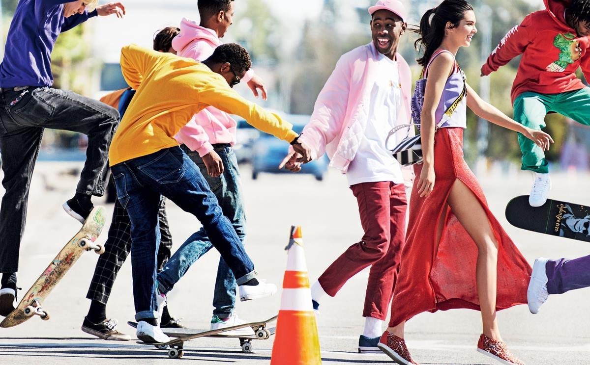 O rapper Tyler, The Creator, um homem negro e jovem, de cabelos raspados, posa para foto do lado da Kendall Jenner. A modelo é uma mulher jovem e branca, de cabelos pretos lisos. Eles estão conversando encostados em uma parede, na rua. - Metrópoles