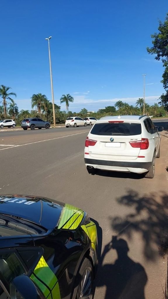 Imagem colorida de uma viatura do Detran-DF e uma BMW branca a sua frente