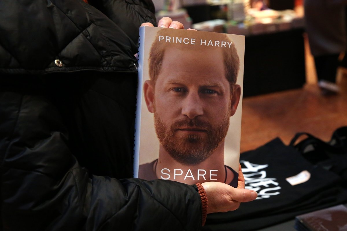 Uma mão branca está segurando o livro do príncipe Harry - Metrópoles