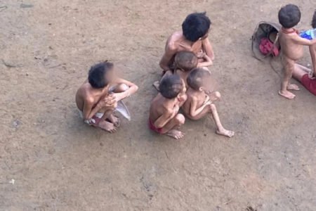 Crianças yanomami desnutridas aparecem sentadas em chão de terra batida em reserva indígena - Metrópoles