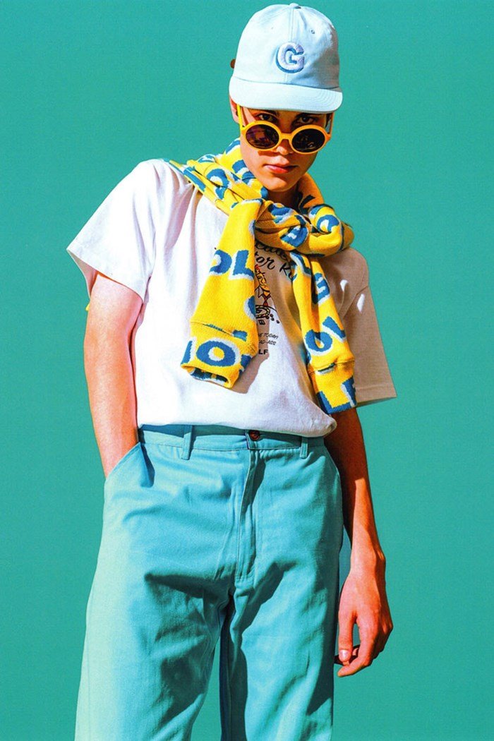Foto de campanha da marca Golf Wang. Na imagem, um modelo branco e jovem faz uma pose e veste uma camiseta branca, uma calça azul, um boné azul e um óculos escuro com armação amarela. - Metrópoles