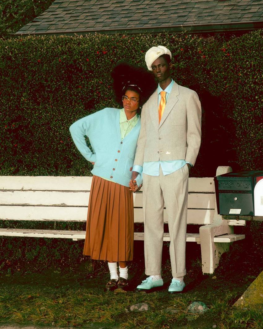 Um homem e uma mulher, ambos jovens e negros, em campanha publicitária da marca GOLF le FLEUR, do rapper Tyler, The Creator. Ela usa uma camisa de botão verde, um casaco cardigã azul e uma saia marrom caramelo. Ele usa uma camisa azul e um terno cinza, além de uma gravata amarela e laranja. - Metrópoles