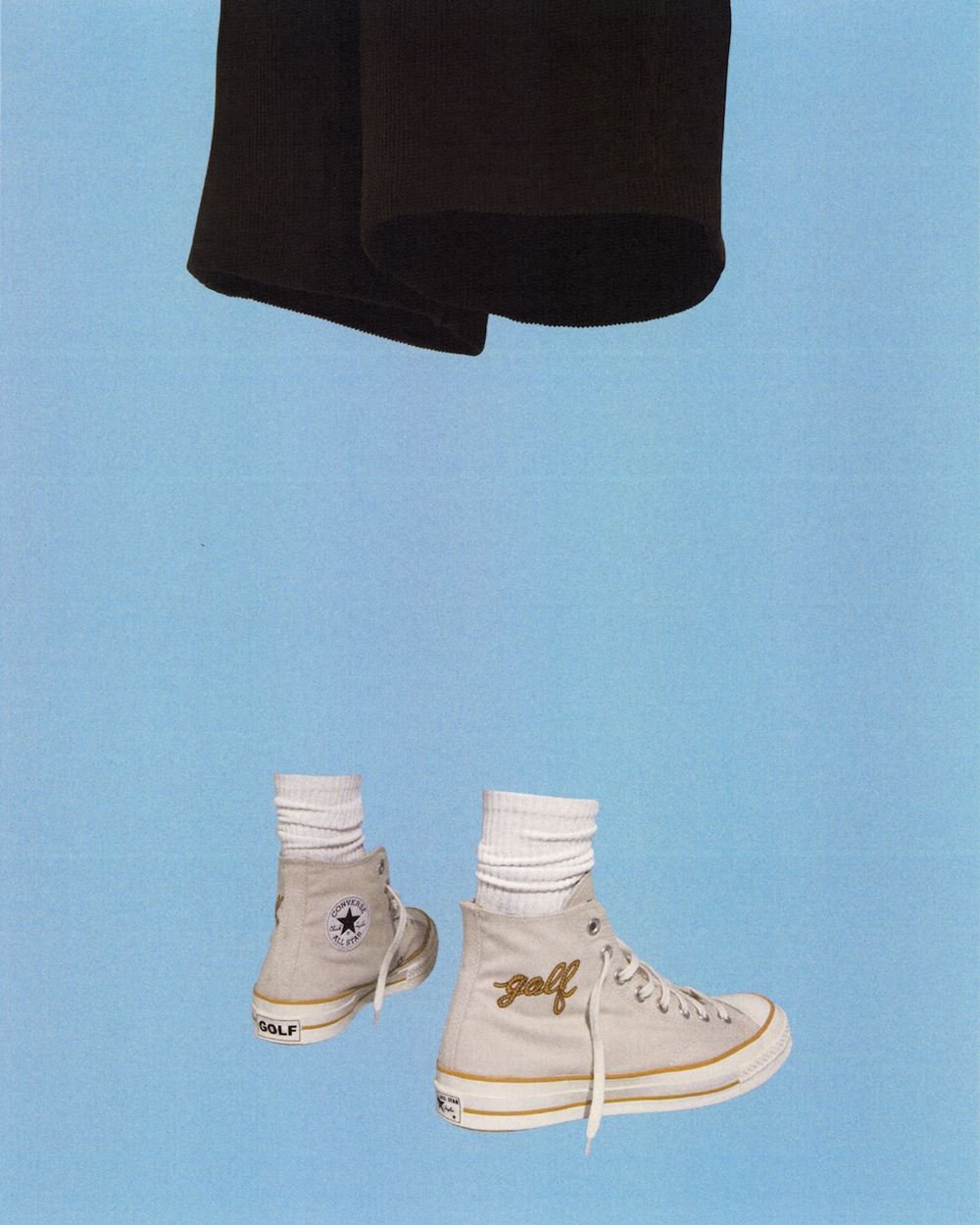 Foto de campanha da marca Converse em que aparece um tênis Chuck Taylor cinza, uma meia branca e uma bermuda preta. - Metrópoles