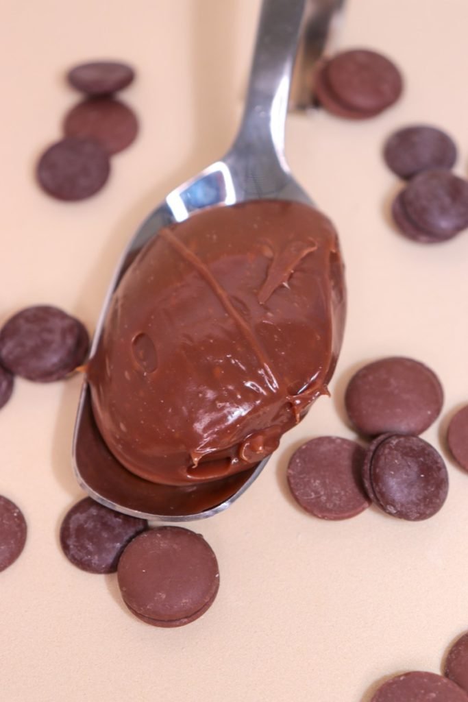 Foto colorida de brigadeiro em colher com gotas de chocolate ao lado - Metrópoles