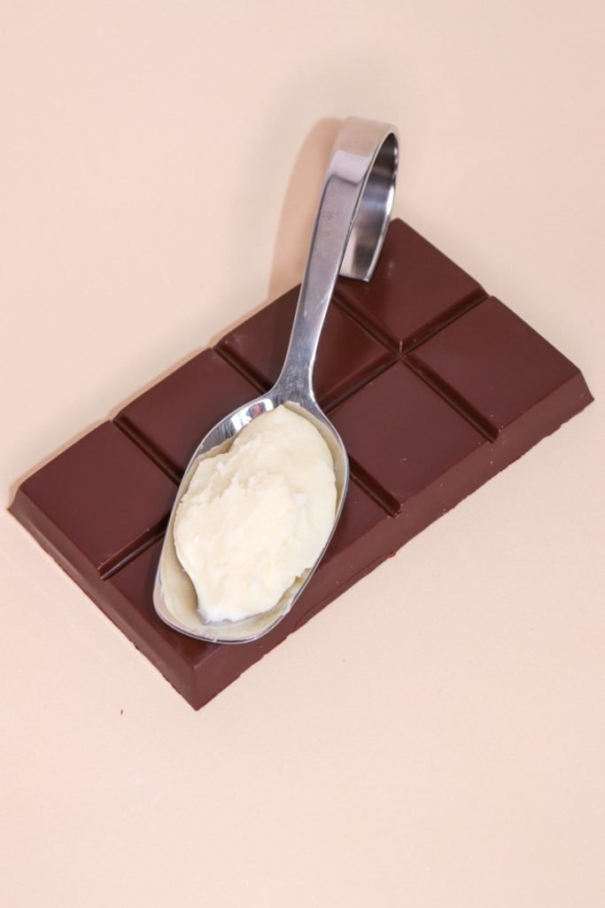 Foto colorida de creme branco em colher, fixada em cima de barra de chocolate - Metrópoles