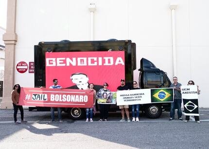 Grupo faz protesto contra o ex-presidente Jair Bolsonaro em Orlando, EUA. Eles seguram faixas com frases de ordem diante de um cartaz com a imagem de Bolsonaro com os dizeres "genocida" - Metrópoles