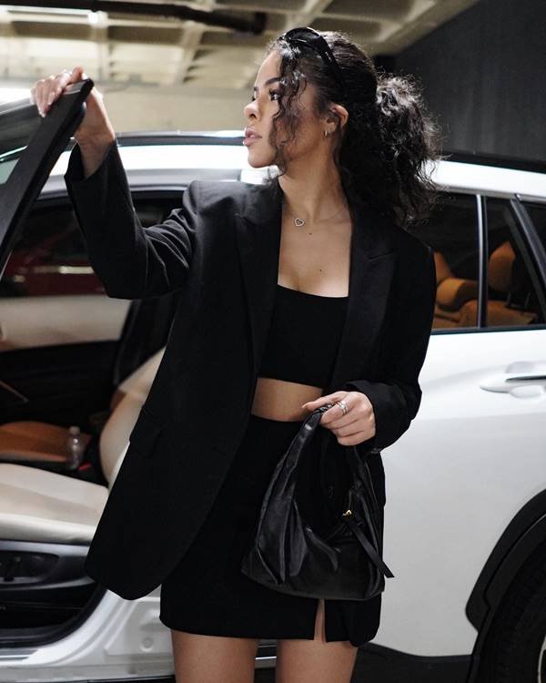 Mulher negra de cabelo cacheado usa top preto e blazer preto - Metrópoles 