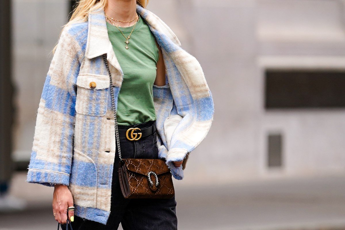 Young Caucasian woman with straight blond hair walking on the street.  She wears a green tank top, black jeans, a white and blue plaid coat and a brown suede Dionysus bag from Gucci.  - Metropolises
