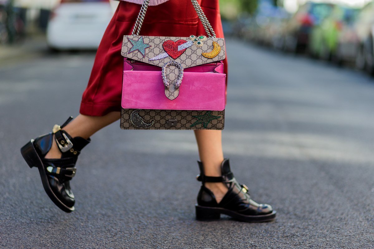 White woman walking on the street.  She is wearing a red dress and a Balenciaga leather bag.  She holds, in one hand, a brown leather bag called Dionysus by Gucci.  - Metropolises