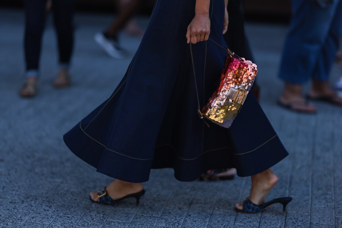 Young black woman walking on the street.  She wears a long dress and jeans, dark heels and Fendi baguettes.  The piece is made of sequins in orange, pink and yellow.  - Metropolises