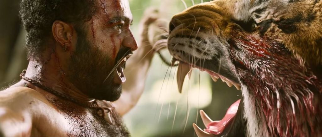 homem pendurado com rosto machucado grita para tigre que ruge - metrópoles