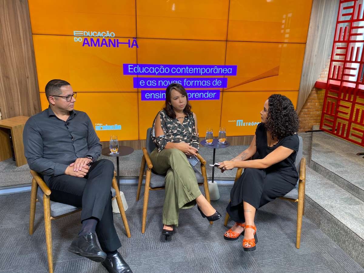 Foto colorida mostrando jornalista de macacão preto e dois entrevistados, um homem e uma mulher, em estúdio-Metrópoles