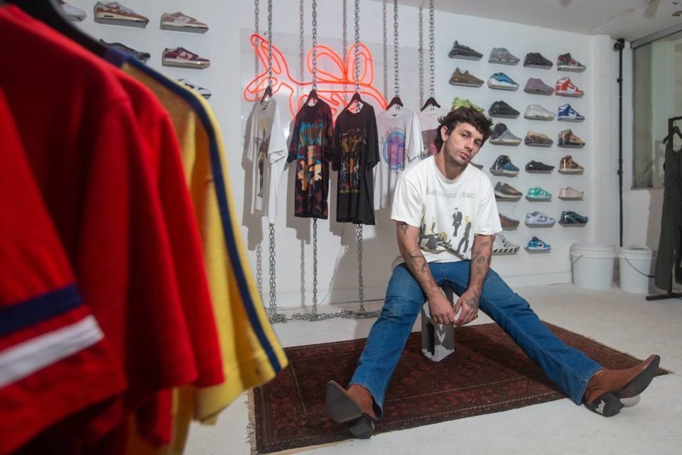 Ulysses Melo, proprietário da Bullseye Vintage, usa calça jeans, camiseta branca e botas e posa com pernas abertas - Metrópoles