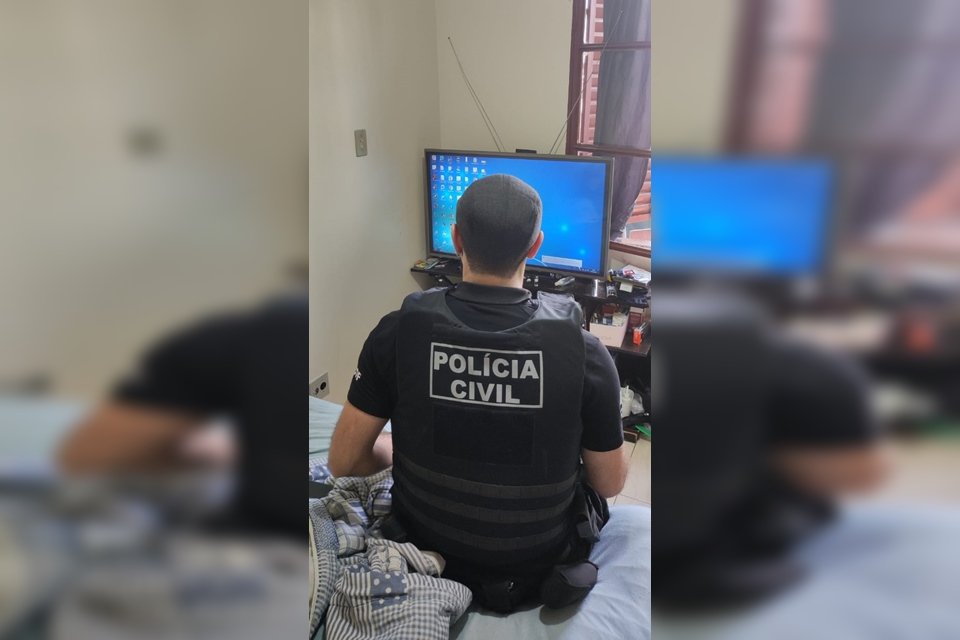Policial fardado de costas, sentado e cama, e olhando para tela de computador