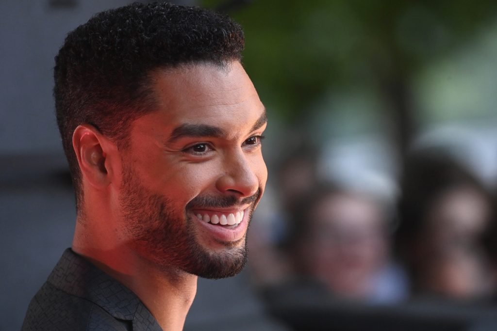 Regé-Jean Page, um homem negro, está olhando para os fotógrafos e sorrindo - Metrópoles