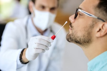 Imagem colorida mostra médico fazendo teste para detecção de covid em um homem que usa óculos