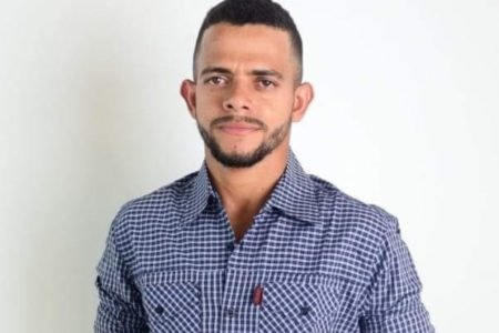 Imagem colorida do vereador Cleidivan Ribeiro Alves, conhecido como Ratim. Ele usa camisa quadriculada azul e branco