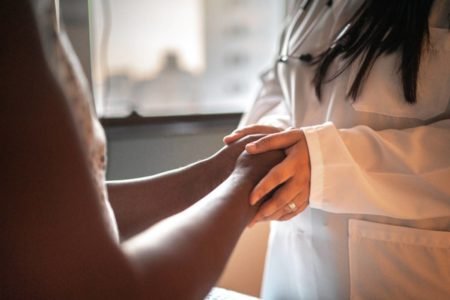Medica segurando mãos de paciente para falar