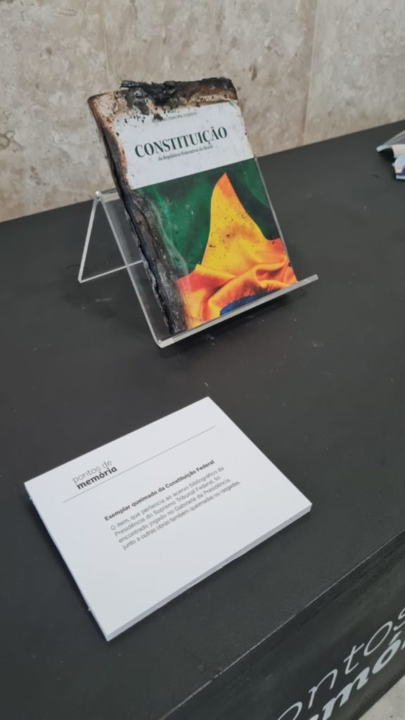 Exposição no plenário do STF com escombros e materiais danificados após invasões antidemocráticas feitas por bolsonaristas em janeiro. No detalhe, exemplar queimado da Constituição com cacos de um objeto quebrado ao lado - Metrópoles