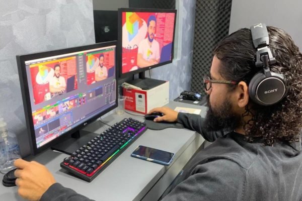 Imagem colorida de um homem de barba mexendo em um computador. Ao seu lado há outro computador