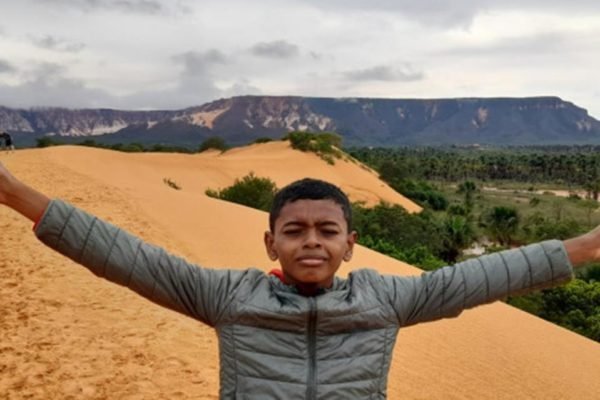 Menino de 12 anos é aprovado em concurso. Na imagem ele aparece em uma duna com os braços abertos - metrópoles