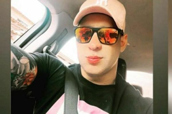 Homem de blusa preta, óculos de sol e boné rosa