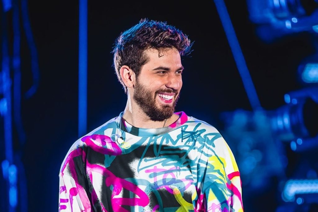 Foto colorida de Gustavo Mioto sorrindo no palco