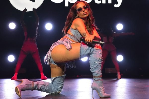 A cantora Anitta, uma mulher jovem, de cabelo ondulado longo, posa para foto durante uma apresentação para o Spotify. Ela usa um look todo jeans, com top, shorts e bota. As peças são da marca Levi's. - Metrópoles
