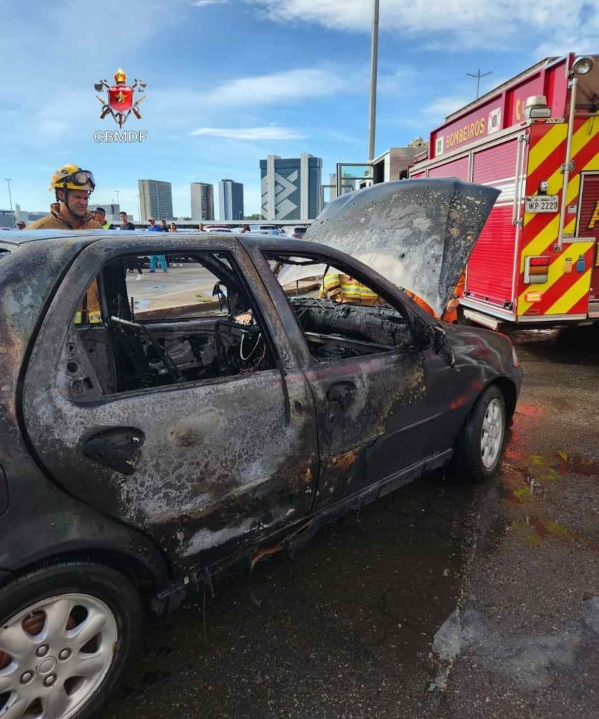 Lateral de Fiat Siena azul com o capô aberto. Carro foi consumido pelas chamas. Foto colorida. Vista diagonal traseira do veículo