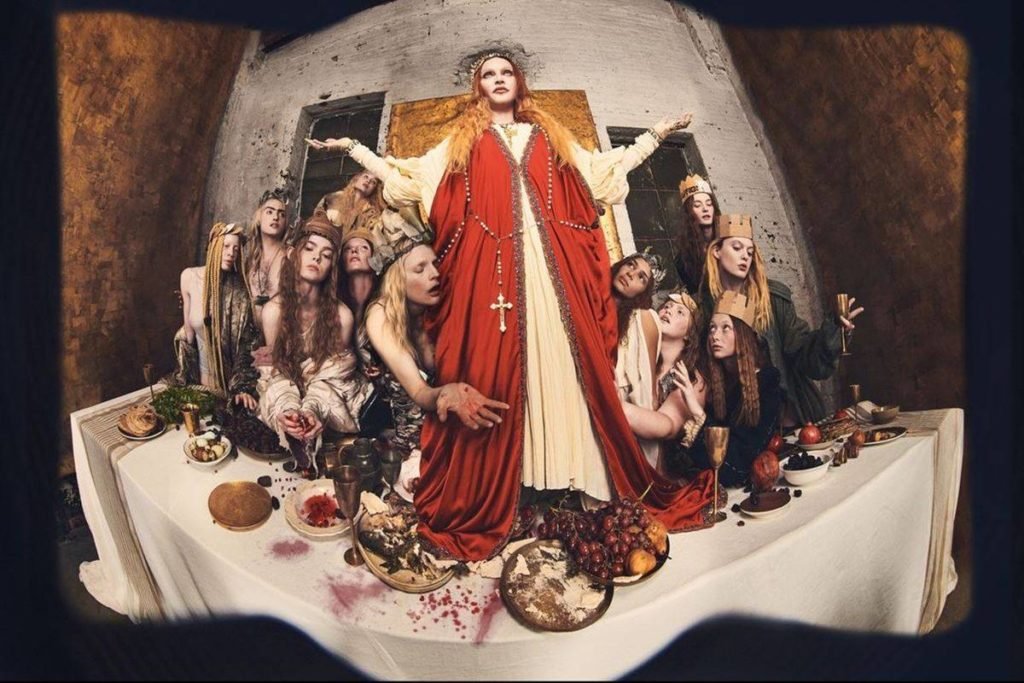 Mulher vestida de Jesus. Ela está em cima da mesa e rodeada por mulheres - Metrópoles