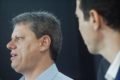 O governador de São Paulo, Tarcísio de Freitas, fala de perfil enquanto homem o assiste - Metrópoles