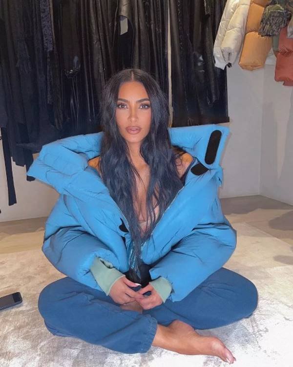 Sentada em uma cama, Kim Kardashian usa casaco azul puffer - Metrópoles