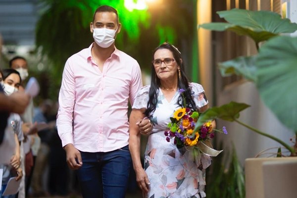 Imagem colorida de um homem usando camisa rosa e calça jeans e uma mulher de vestido florido