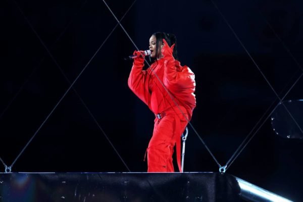 Rihanna cantando. Ela está utilizando uma roupa vermelha e mostra a barriga de grávida - metrópoles