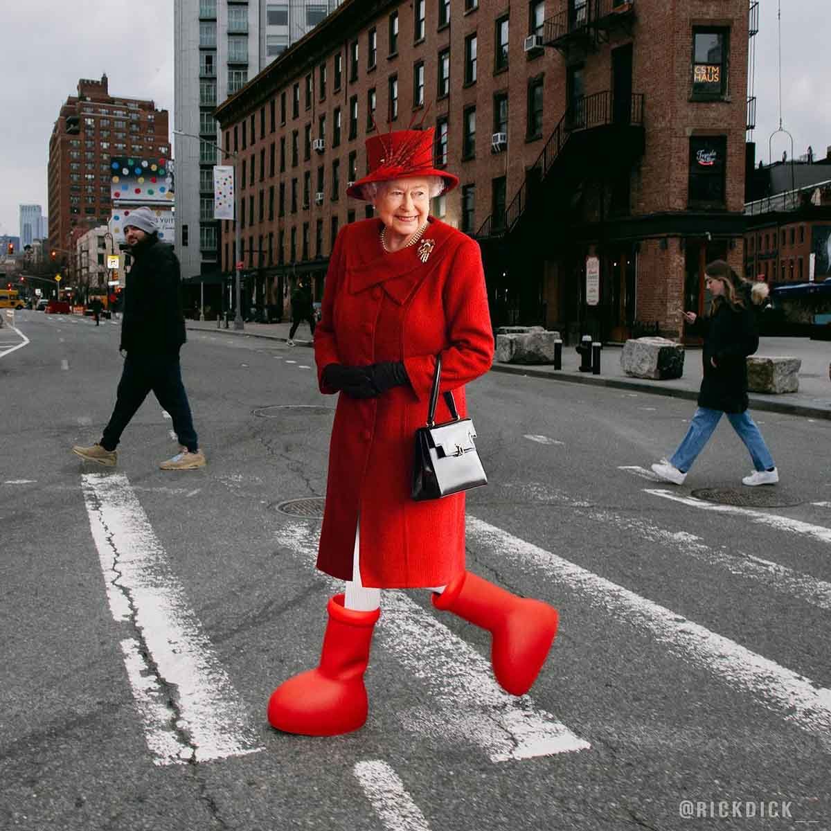 A rainha Elizabeth andando pelas ruas de Nova York. Ela é uma senhora idosa branca, com cabelos curtos também brancos, e usa um casaco vermelho e a bota vermelha gigante de plástico da marca MSCHF. - Metrópoles